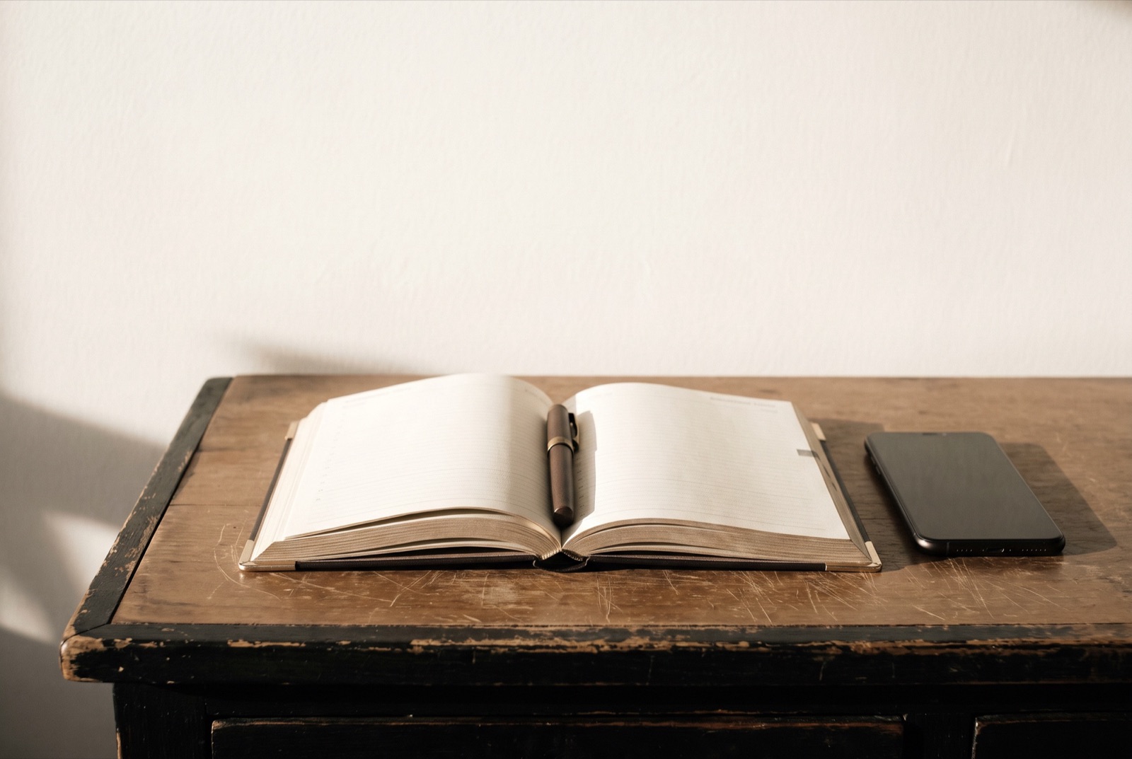 An open appointment calendar on a worn counter, a pen laid in the gutter between the pages and a phone face down beside it.